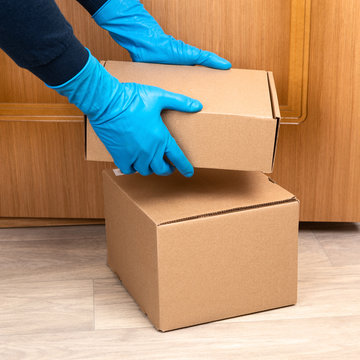Contact less delivery concept, touch free shipment, courier in a protective mask and rubber gloves with carboard box , safe order from online shop