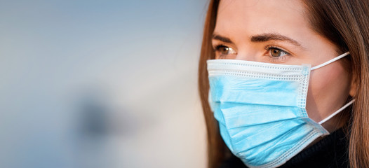 Young woman wearing disposable blue virus face mouth nose mask, closeup portrait - wide banner with...
