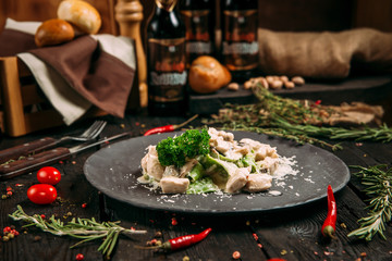 Side view on alfredo pasta with parmesan on a black plate on the dark wooden background, horizontal