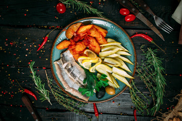 Russian snack for alcohol with potatoes, pickles and herring in a blue plate on the black wooden background, top view, horizontal