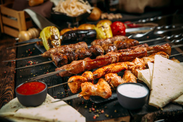 appetizing assorted set kebab sticks with red sauce and pickled onion on a black board on a dark wooden background, side view, vertical
