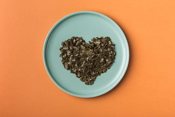 Hemp flakes in a flat dish in the form of a heart on an orange background.