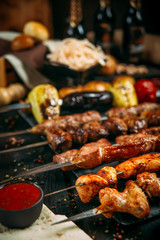 appetizing assorted set kebab sticks with red sauce and pickled onion on a black board on a dark wooden background, side view, vertical