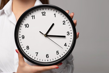 cropped view of young businesswoman in white shirt holding clock isolated on grey background  