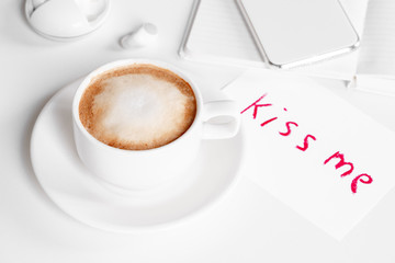 White cup of cappuccino and note written by lipstick kiss me. Romantic relations and flirt concept