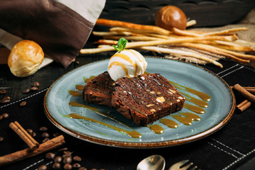 appetizing chocolate brownie with vanilla ice cream on a plate on the wooden table with decoratice elements, horizontal
