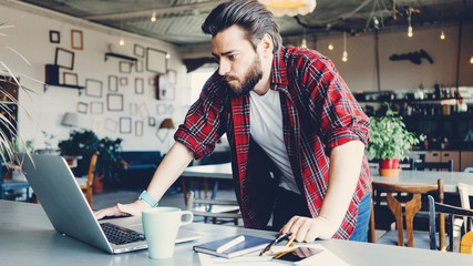 Excited man working with laptop. Entrepreneur wearing casual clothes and stubble in big spacious bright room. Workspace on the table