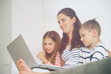 happy young family mother with laptop sitting on sofa with two beautiful kids during home leisure self isolation quarantine