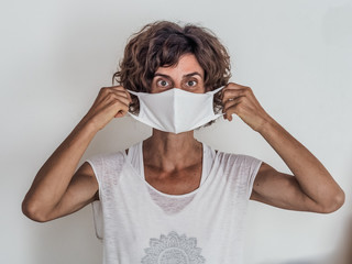 woman protecting from corona virus covid-19 putting on a white medical face mask on neutral...