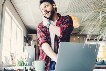 Young man working with laptop. Entrepreneur wearing casual clothes and stubble in big spacious bright room. Workspace on the table. Talking on mobile phone
