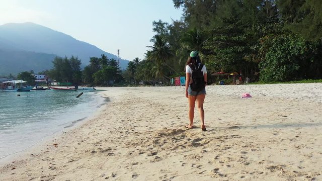 Traveler girl with backpack walking on sandy exotic beach alongside calm sea water toward vacations resort in Vietnam