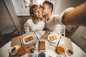 Romantic couple taking a selfie at breakfast in the kitchen at home. Beautiful people at quarantine period.