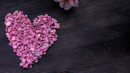 Decorative pink heart, small box with a gift and ribbon and flowers on a dark wooden background