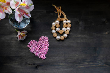 Romantic bunch of spring dark pink heart, beads and flowers on a dark wooden background