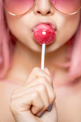 Cropped portrait of a sensual attractive girl holding pink lollipop in her lips. Selective focus