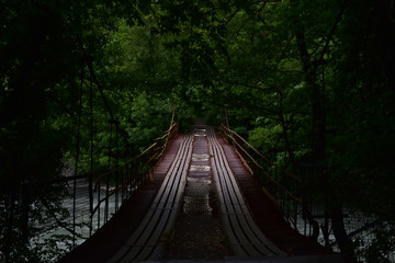 Dark old and moody iron bridge over the river with bushy trees along it