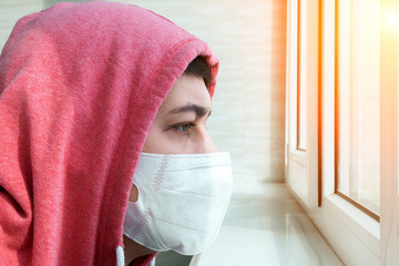 young man in a protective mask at home outside the window.