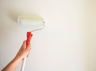 male hand painting wall with paint roller. Painting apartment, renovating with white color paint