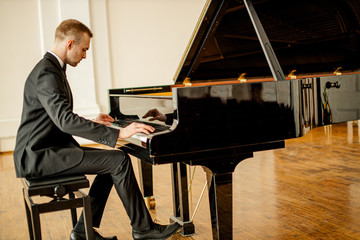 young handsome caucasian man in formal elegant suit gracefully play piano. professional pianist perform classic music - obrazy, fototapety, plakaty