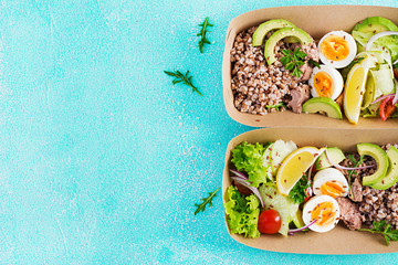 Healthy food delivery. Lunch- Buckwheat porridge, sliced tuna, boiled egg and fresh vegetable salad in zero waste containers  on blue background. Top view, flat lay