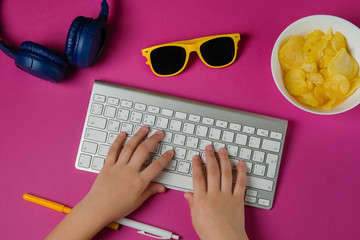 Flat lay of keyboard, headphones, sunglasses, pen, and a plate of chips in purple background. Concept of a teenager, blogger, student. Top view.