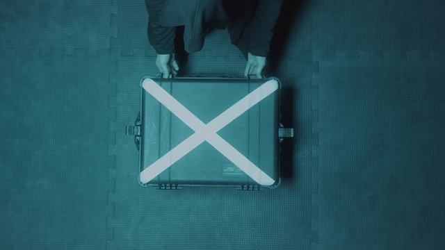 Top view of a hacker man wearing hood opening silver suitcase with a white cross. Stock footage. Mysterious case that lying on concrete surface being opened by a man.