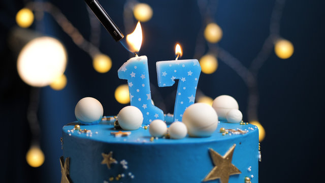 Birthday cake number 17 stars sky and moon concept, blue candle is fire by lighter. Copy space on right side of screen. Close-up