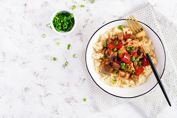 Bulgur and sauteed chicken, mushrooms, eggplants, paprika and tomatoes in a white bowl. Top view, overhead