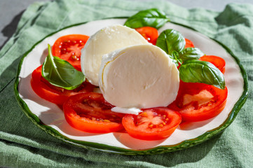 Tasty italian fresh salad with white soft cheese mozzarella ball, red tomatoes and fresh green basil