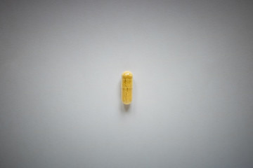 one yellow pill on a plain background