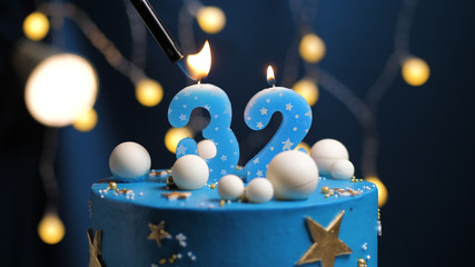 Birthday cake number 32 stars sky and moon concept, blue candle is fire by lighter. Copy space on right side of screen. Close-up