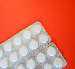 white pills on a red background. snow-white round antibiotics against viruses.
