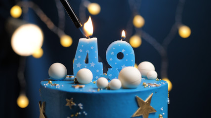 Birthday cake number 49 stars sky and moon concept, blue candle is fire by lighter. Copy space on right side of screen. Close-up