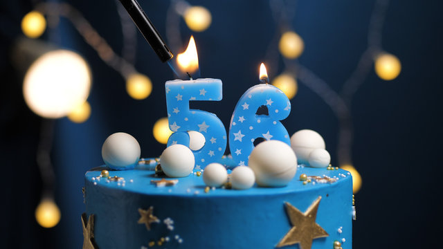 Birthday cake number 56 stars sky and moon concept, blue candle is fire by lighter. Copy space on right side of screen. Close-up
