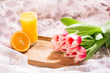 Orange juice in bed on a wooden tray and white-pink bouquet of fresh cut tulips