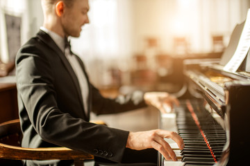 gorgeous caucasian male pianist on a stage, man in elegant suit perform classical music for...