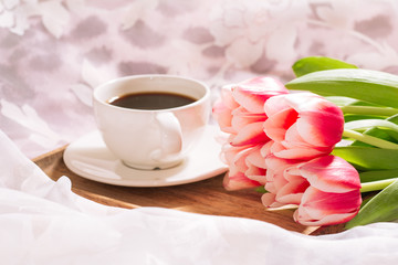 Fototapeta na wymiar A cup of aromatic freshly ground coffee with a fresh bouquet of white-pink tulips on a wooden tray. Horizontal view