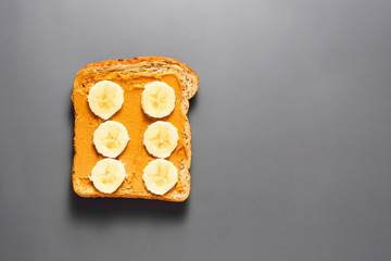 Peanut butter and banana toast over grey background. Top view. Copy space.