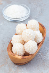 Homemade healthy raw paleo energy balls with shredded coconut, almond flour, coconut butter and sweetener in wooden bowl, vertical