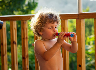 Little boy plays on a nozzle. The child learns music. A child plays a wooden flute outdoor.