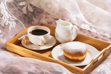 Breakfast in bed with freshly brewed and aromatic coffee, cane sugar, jug of cold milk and doughnut in powdered sugar on a wooden tray