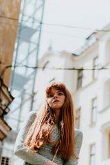 Fototapeta premium Stylish urban young redhair woman in a fashionable green dress posing in the street. European modern cute model girl enjoys a walk in the city. Spring fashion.