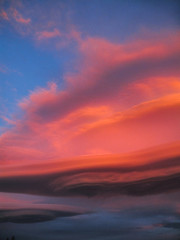 Fototapeta na wymiar Pnk orange lenticular clouds form in the sky at sunset