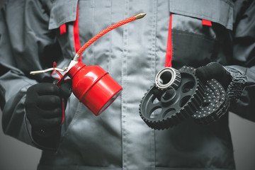Auto mechanic holding in hands a red oil can and car parts on dark background.