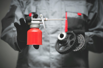 Auto mechanic holding in hands a red oil can and car parts on dark background.