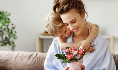 Little boy embracing happy woman with bouquet of colorful flowers.