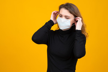 Coronavirus. Girl puts on a protective mask. Female student in a medical mask on a yellow background. Epidemic. Fever in China. Concept - girl is afraid of illness. Virus protection.