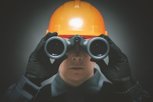 Builder Worker Is Looking Through A Binoculars In His Hands Close Up.