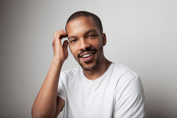 Close-up portrait of young black man wearing T-shirt against white wall with happy face.