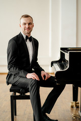 talented caucasian male pianist sit, look at camera and smile. professional classical music performer before performance on a stage